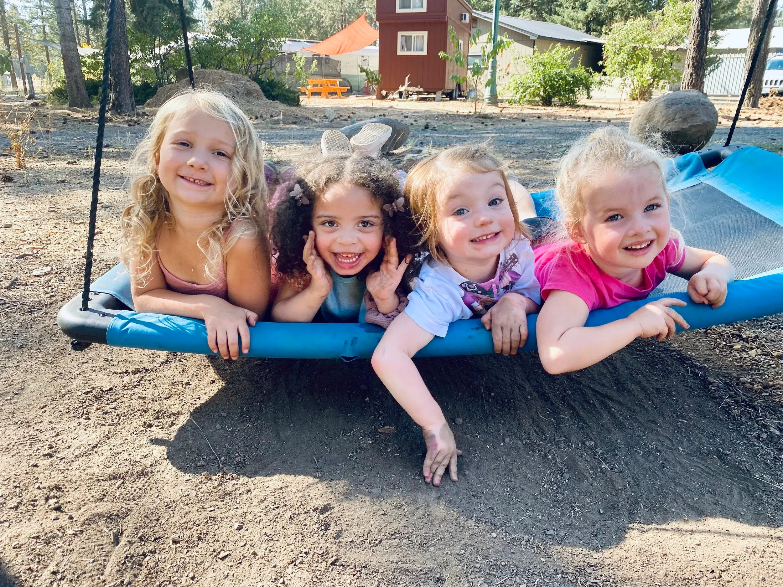 Four smiling children lying side by side on a tire swing