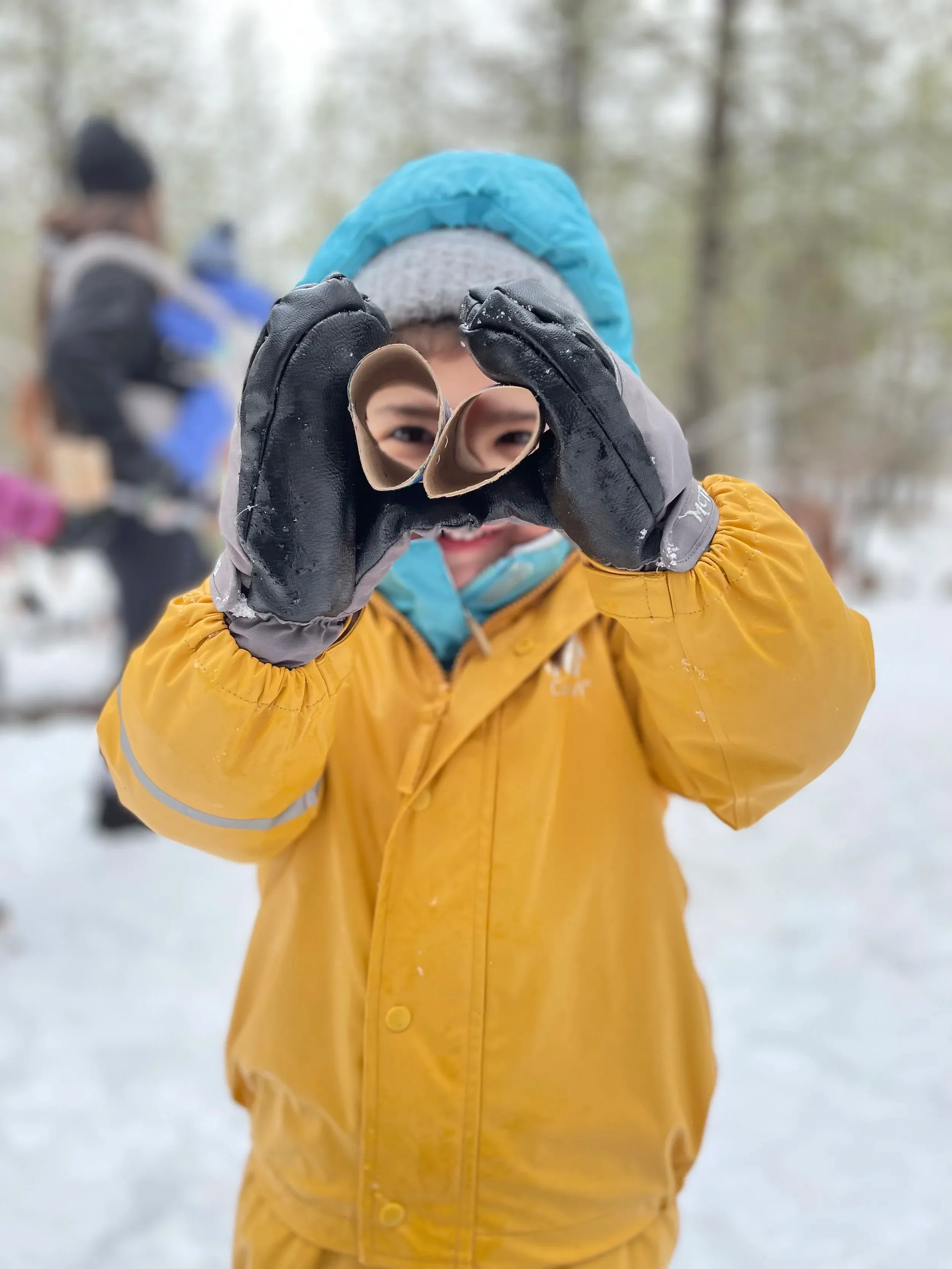 A child in yellow rain gear looking through toy binoculars