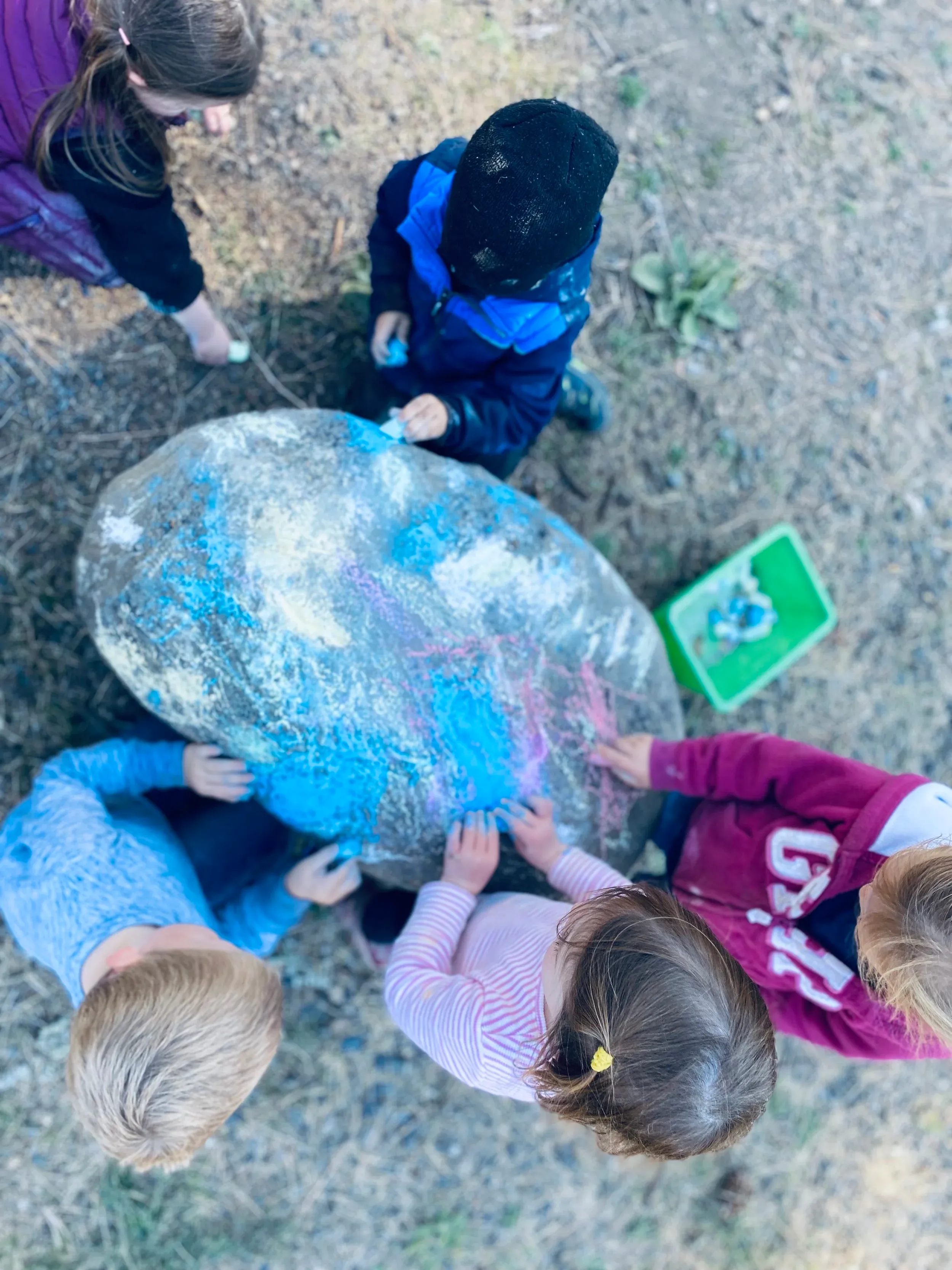Children gathered around painting a big rock